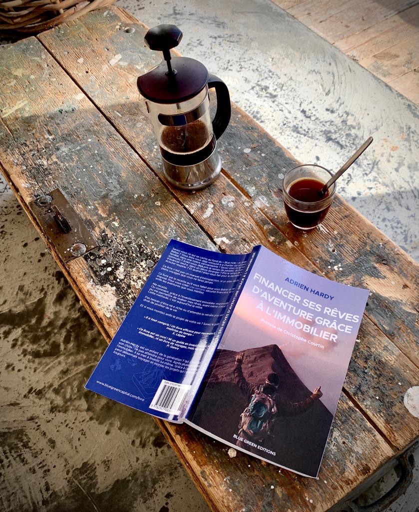 Le livre Financer ses rêves d'aventure grâce à l'immobilier d'Adrien Hardy posé sur une table en bois avec une cafetière